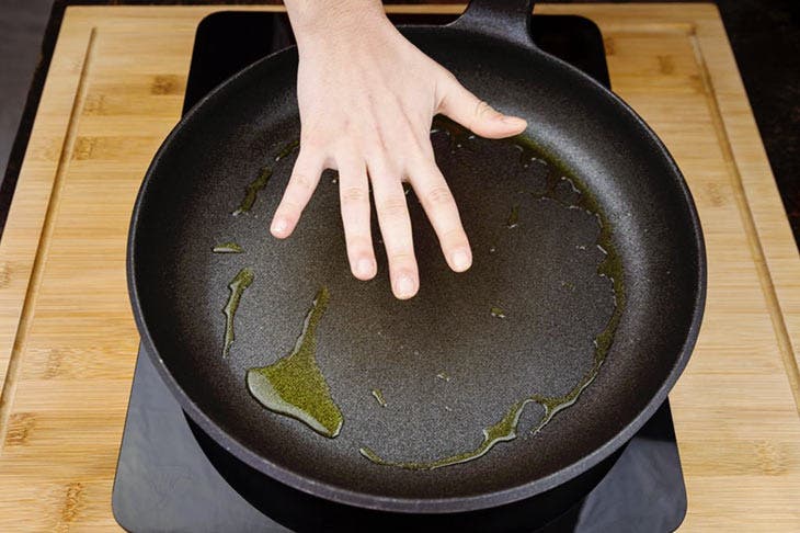 Una mano midiendo la temperatura de una sartén impregnada con aceite de cocina